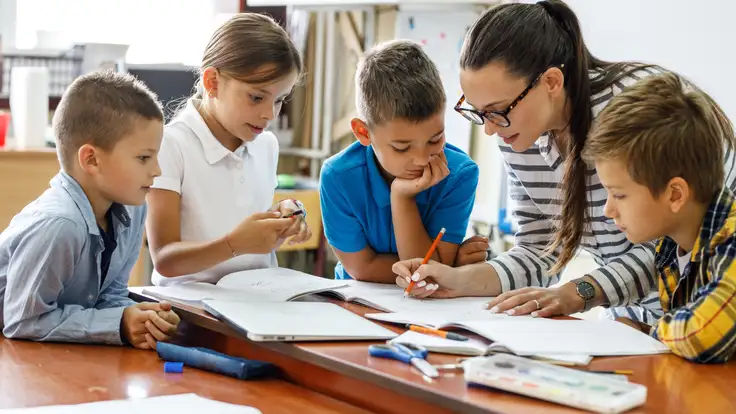 Una maestra experta en educación y pedagogía en un salón de clases dibujando con a niños observando a su alrededor