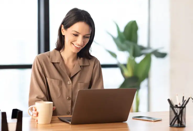 Mujer joven estudiando en línea con una laptop en una cafetería, usando audífonos y sonriendo durante una videollamada. Representa el concepto de educación personalizada desde casa