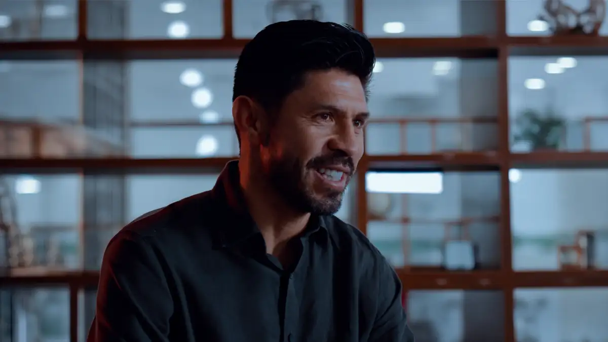 Primer plano de Oribe Peralta hablando durante una entrevista, vistiendo una camisa oscura en un espacio interior iluminado.