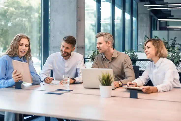 Equipo de trabajo diverso colaborando en una mesa de oficina, simbolizando el liderazgo horizontal y la colaboración en entornos laborales modernos. 